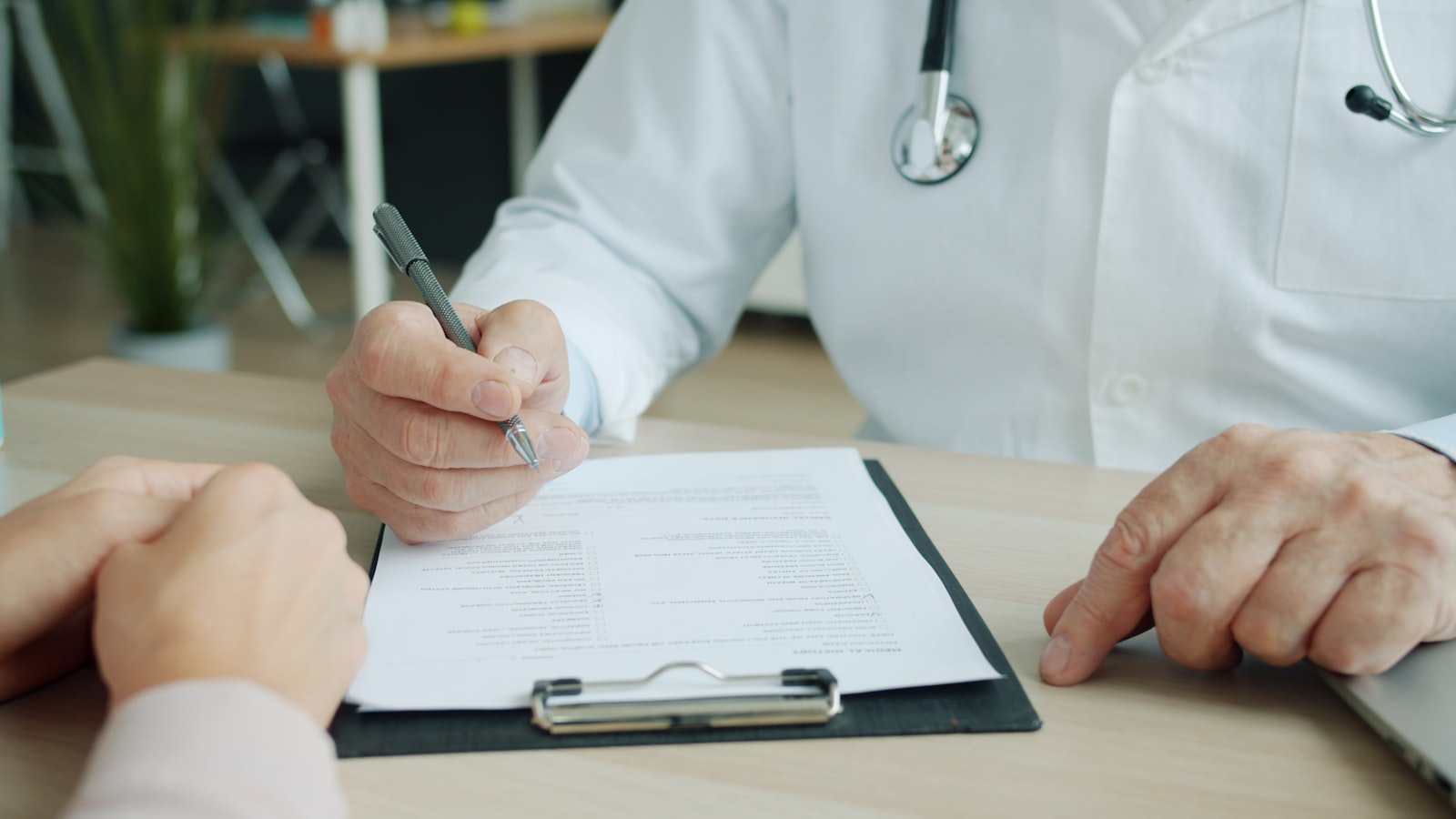 Ein Arzt füllt während einer Sprechstunde eine Krankenakte aus