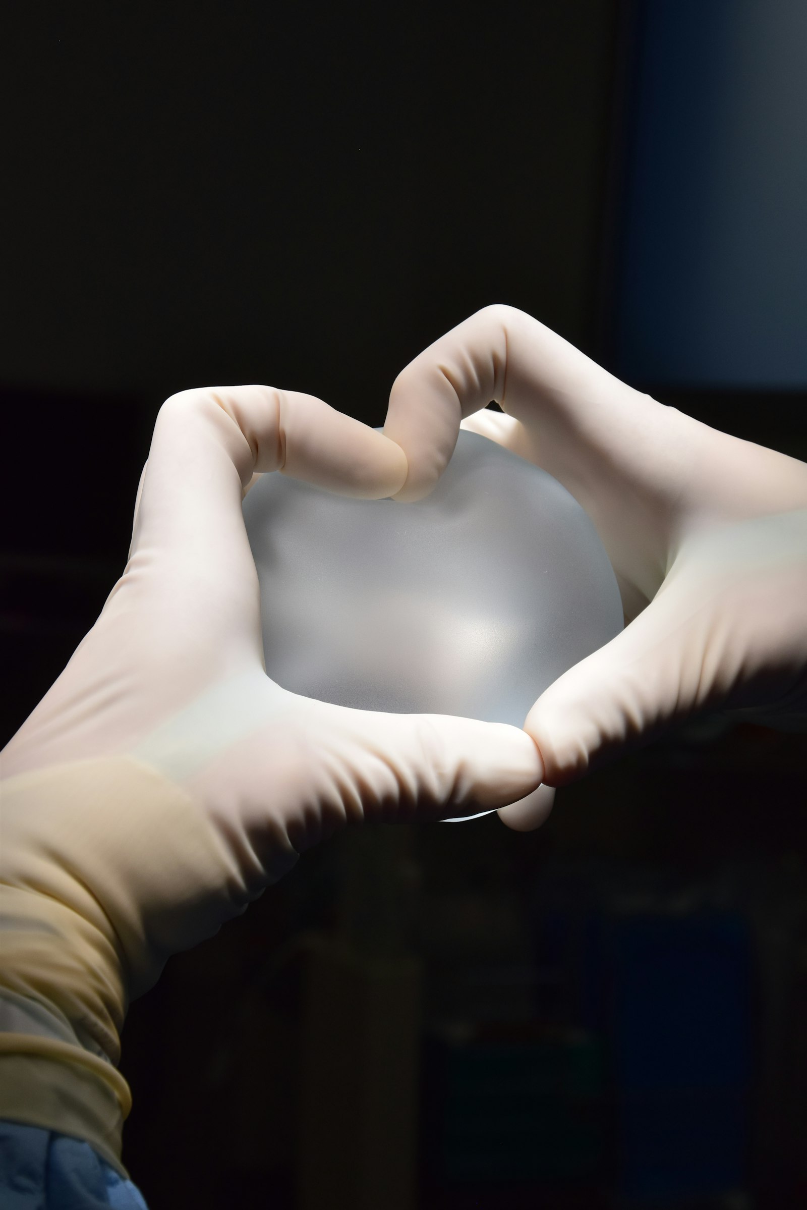 Mani guantate che tengono una protesi mammaria in silicone