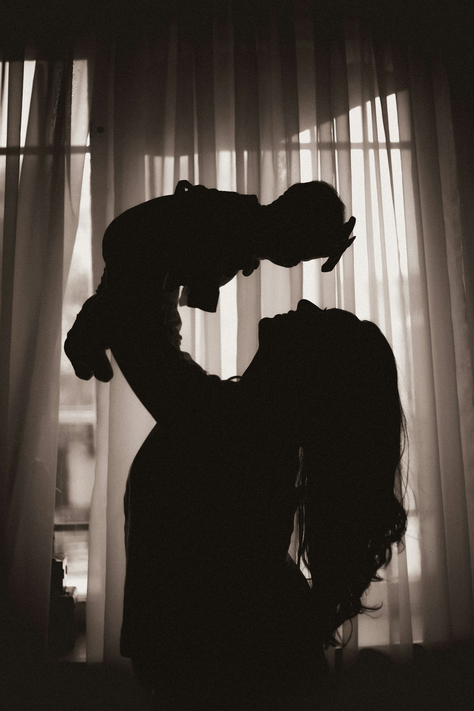 Silhouette di una madre che solleva il suo bambino davanti a una finestra